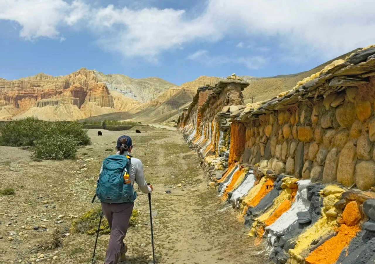 Trekker walking past a colorful Mani wall and enjoying the scenery on the Upper Mustang Trek