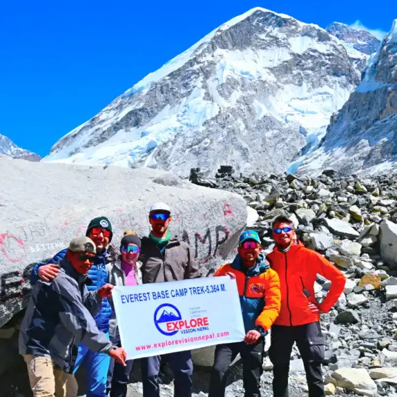 Luxury Everest Base Camp Trek group at Everest Base Camp with the iconic EBC rock and Himalayan mountains with Khumbu ice fall in the background